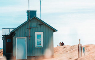 A couple sits near a small house on the beach