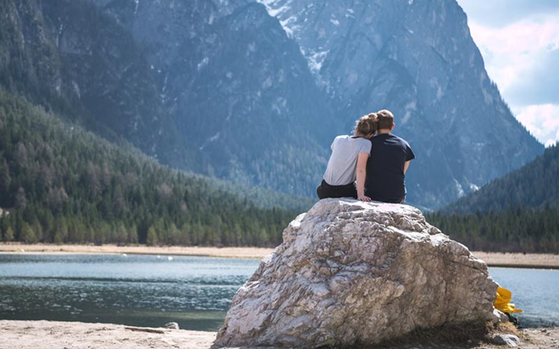 A couple sitting calmly on a rock looking out over a lake at trees