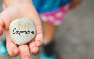 Child's hand holding a rock engraved with the word 'Cooperative'