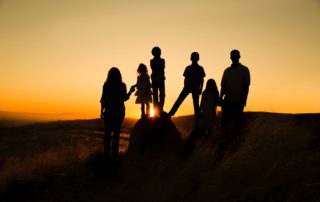 Family of six standing on a rock in front of a sunset – dark figures