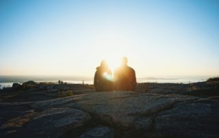 Couple sitting peacefully on rocks at the beach with the sun behind them