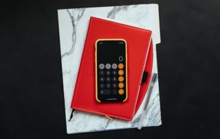 A phone opened to a calculator on top of a notebook that's on top of a folder on a table
