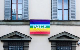Four windows with shutters and arches with a rainbow flag in the center that reads 'Pace'